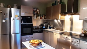 A kitchen with stainless steel appliances, a white countertop, and a table with a fruit bowl. - Provencal-style farmhouse with charm, swimming pool, and landscaped grounds on 6,200 m² (Draguignan)