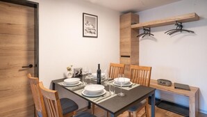 Un comedor con una mesa preparada para cuatro, sillas, un banco de madera, un perchero y un cuadro en la pared.