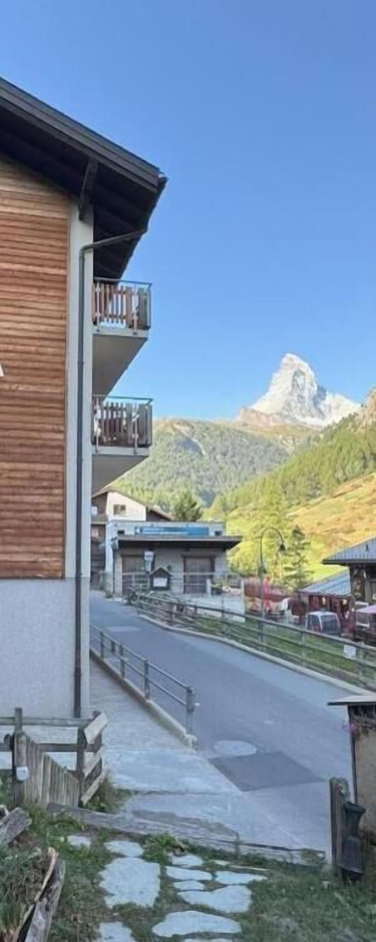 Ein Gebäude mit Balkon, eine Straße im Vordergrund und ein Berg im Hintergrund.