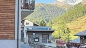 Un edificio con balcón, una carretera al frente y una montaña al fondo.