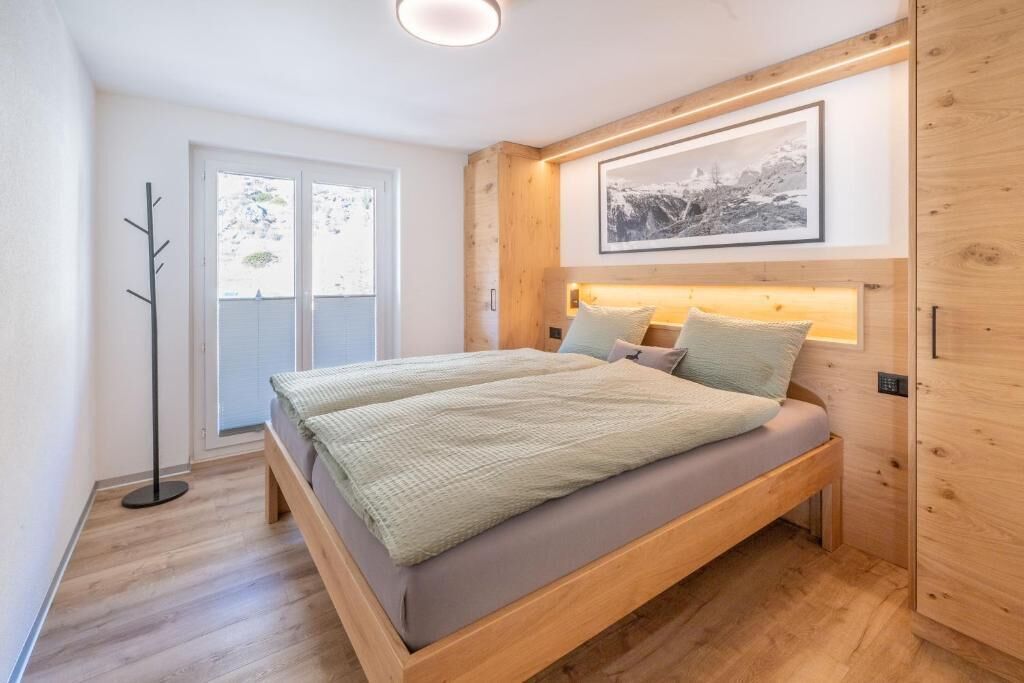 A bedroom with a bed, a floor lamp, a framed picture on the wall, and a window.