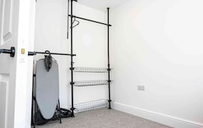 Ein Zimmer mit einer schwarzen Metallregaleinheit an einer weißen Wand, darin ein Staubsauger und ein graues Bügelbrett.