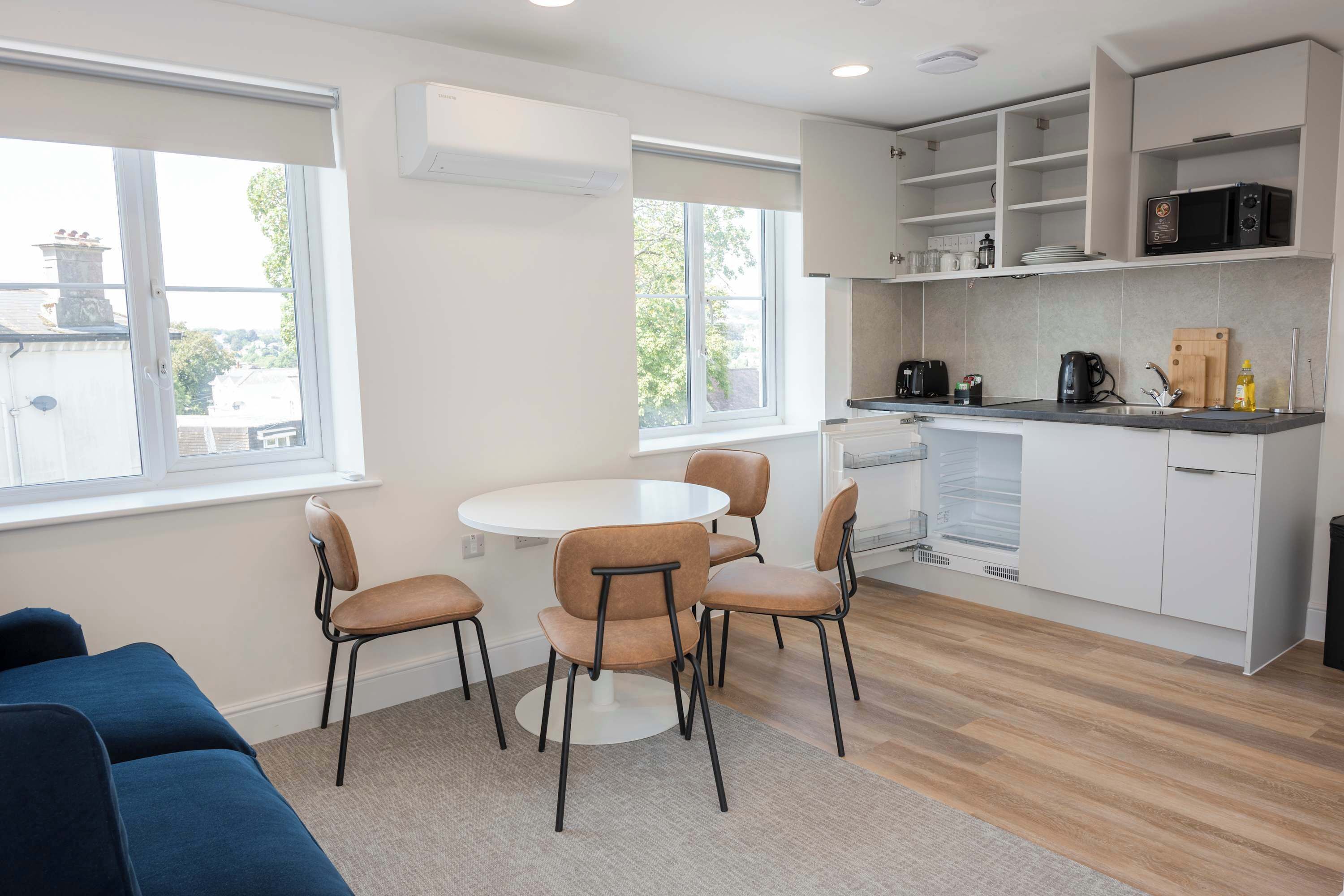 A modern kitchen with white cabinets, a black microwave, and a coffee maker. There is a round table with four chairs in the center.