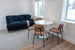 A room with a dark blue sofa, a round white table, and four chairs.