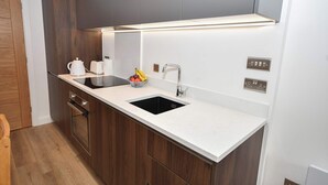 Une cuisine moderne avec un plan de travail blanc, des meubles de cuisine en bois foncé, un évier noir et un robinet en acier inoxydable.