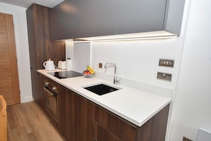 Eine moderne Küche mit weißer Arbeitsplatte, dunklen Holzschränken, einem schwarzen Spülbecken und einem Edelstahlarmaturen.