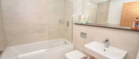 A modern bathroom with a glass-enclosed shower, a white bathtub, a toilet, and a sink.