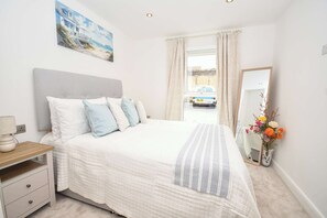 A bedroom with a bed, bedside table, lamp, curtains, a mirror, and a painting on the wall. - Modern 1 Bed Apartment in Central Leeds - Sleeps 3 (Leeds)