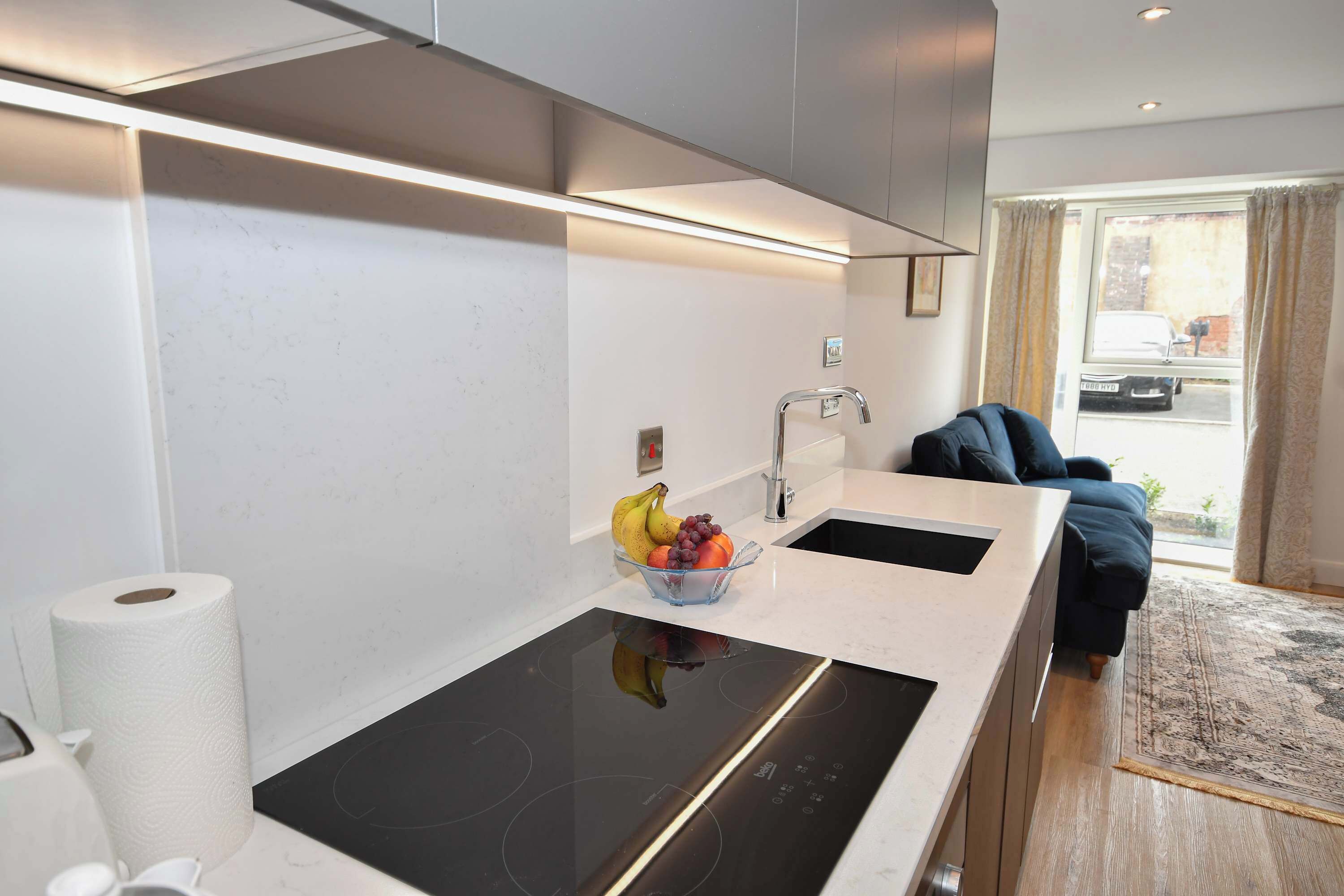Une cuisine moderne dotée d’une cuisinière intégrée, de deux éviers et d’un panier à fruits posé sur le plan de travail.