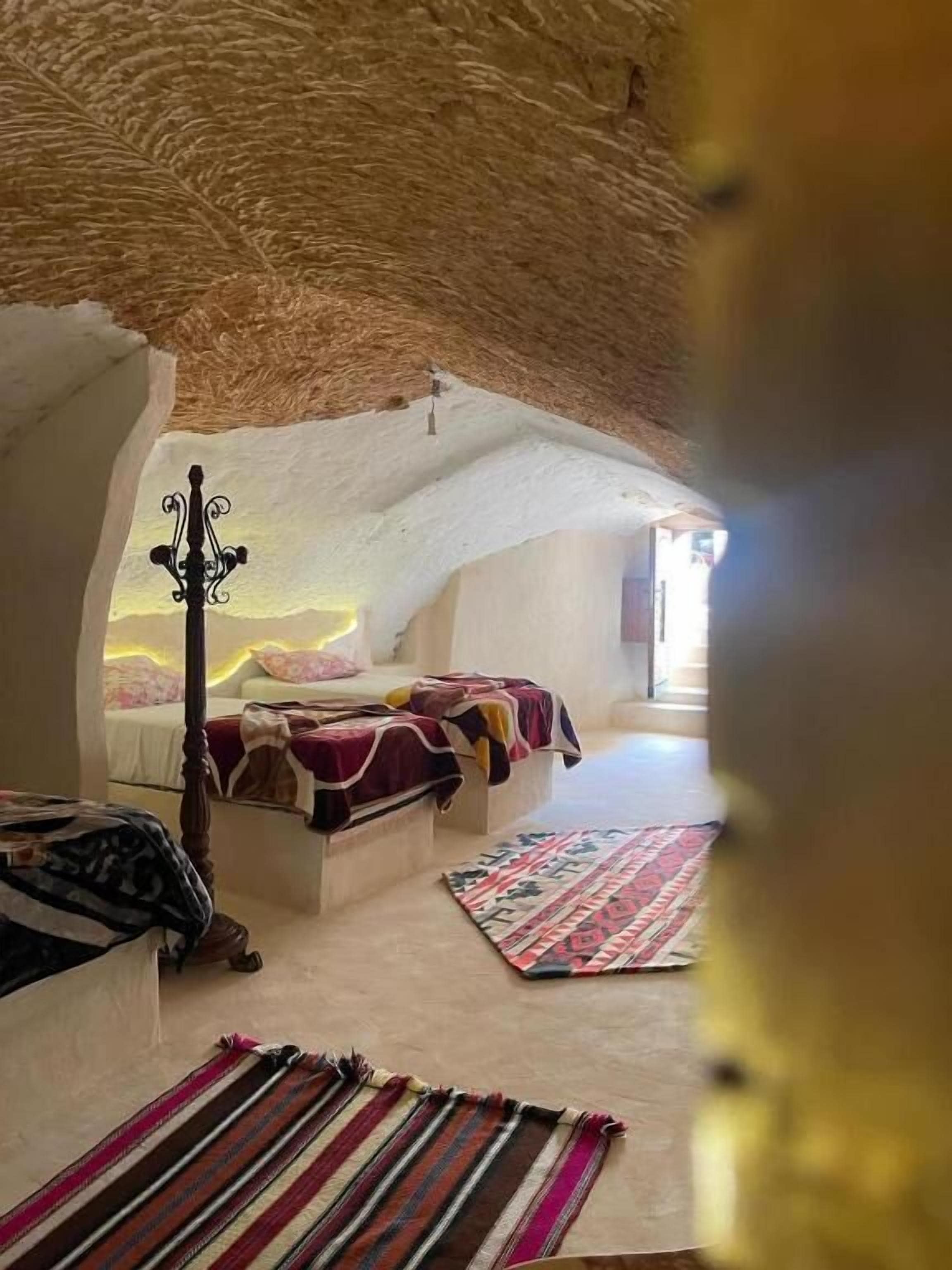 Un dormitorio acogedor con techo de paja, una cama con manta estampada y una mesita de noche con lámpara.