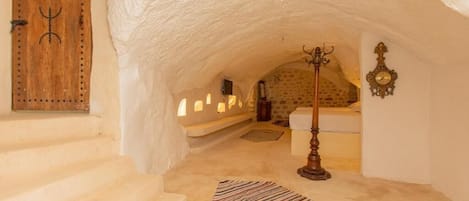 Un interior con pared de piedra, puerta de madera, alfombra estampada y lámpara de pie de madera.