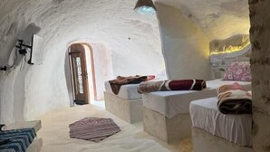 Een interieur met een hoge gewelfde plafond, een bed met kussens, een bankje, en een hanglamp.