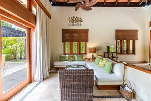 Quarto com sofá, uma poltrona de vime, televisão e janela com vista para o verde.