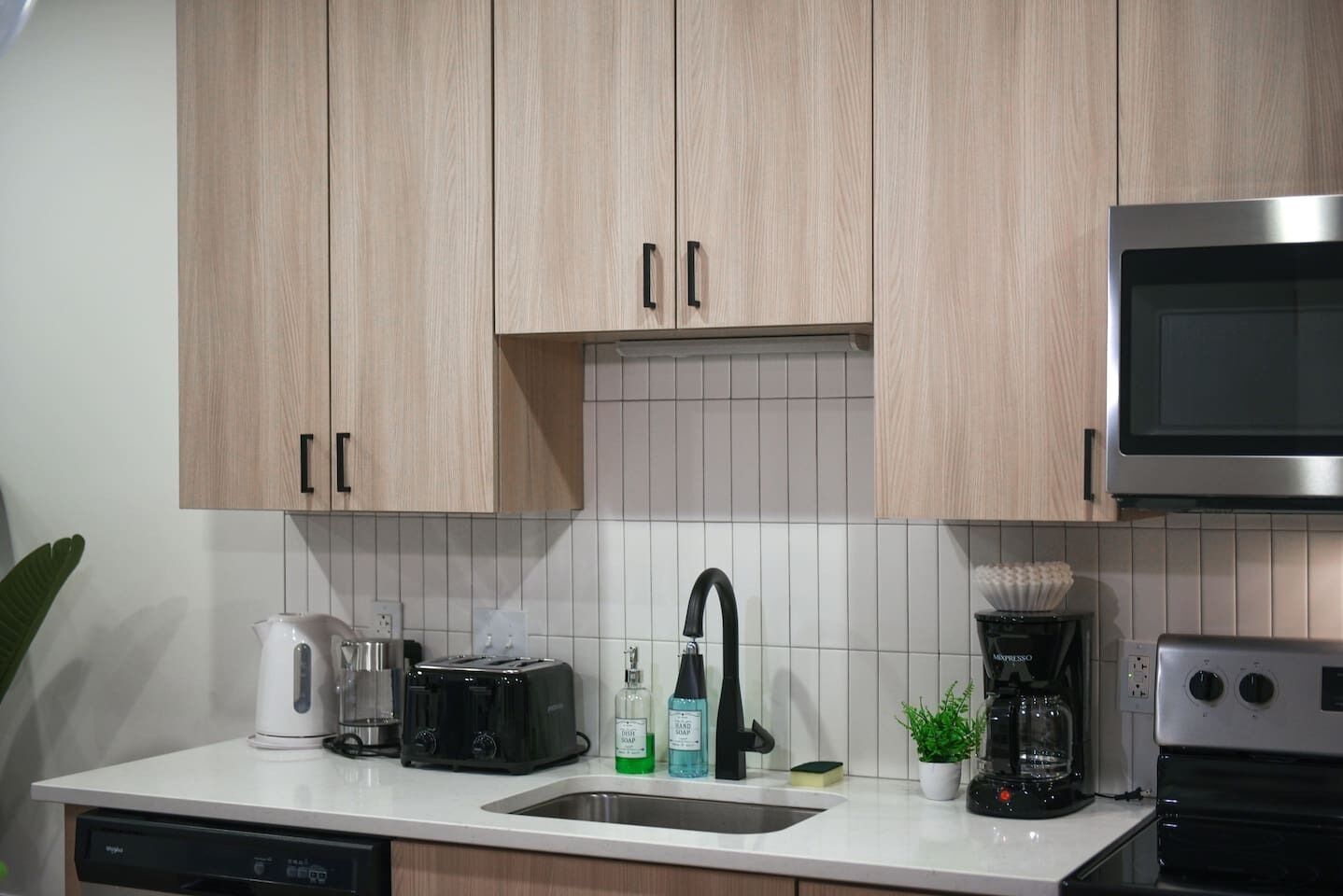 Una cocina con armarios de madera, microondas, cafetera, tostadora y lavavajillas.