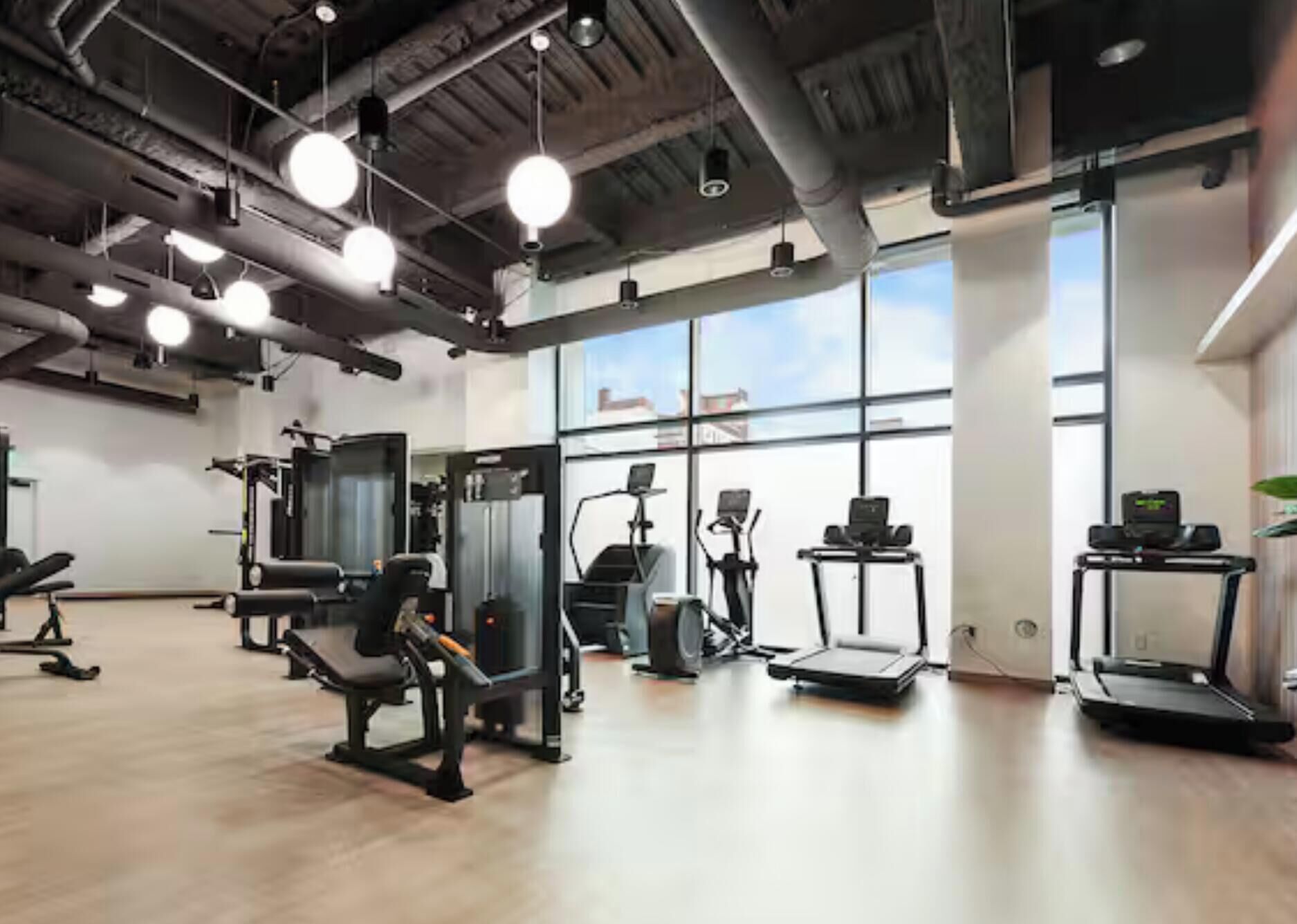 A gym with exercise equipment, large windows, and a high ceiling.