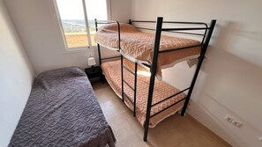 A bunk bed with a lower bunk and a single bed, both with patterned bedding. There is a window with a view of buildings outside. - Quiet 2-bedroom chalet in Vera Playa | Pool & Near the beach (Vera)