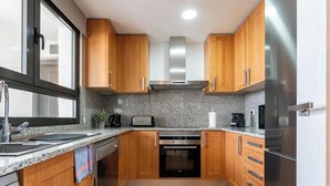 A compact kitchen with wooden cabinets, a stainless steel range hood, a built-in oven, a refrigerator, and granite countertops. - Estepona Duplex with BBQ & Jacuzzi (Estepona)