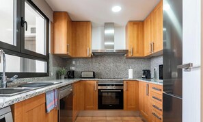 A compact kitchen with wooden cabinets, a stainless steel range hood, a built-in oven, a refrigerator, and granite countertops. - Estepona Duplex with BBQ & Jacuzzi (Estepona)