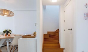 A modern interior with a wooden staircase, a dining area with a table and chairs, and a hanging light fixture. - Estepona Duplex with BBQ & Jacuzzi (Estepona)