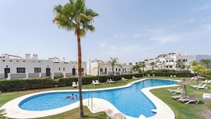 A swimming pool with lounge chairs, palm trees, and modern buildings in the background. - Estepona Duplex with BBQ & Jacuzzi (Estepona)