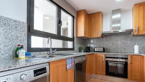 A modern kitchen with granite countertops, stainless steel appliances, wooden cabinets, and a large window. - Estepona Duplex with BBQ & Jacuzzi (Estepona)