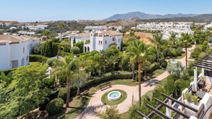 A residential area with white buildings, a circular garden with a fountain, and a clear blue sky. - Estepona Duplex with BBQ & Jacuzzi (Estepona)