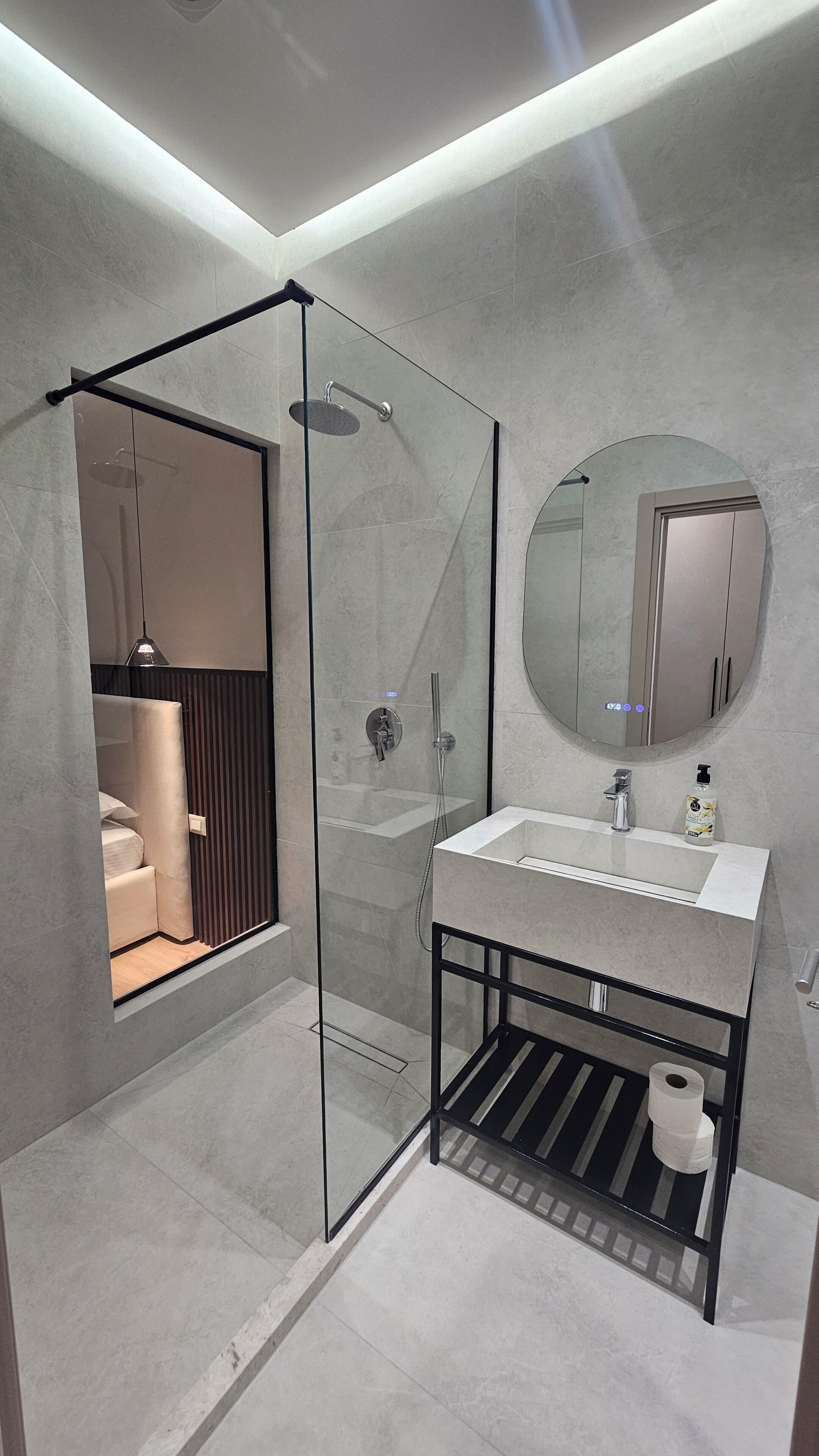 A modern bathroom with a glass-enclosed shower, a round mirror, and a white sink.
