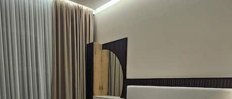 A modern hotel room with a large bed, a bedside table, a mirror, and a window with curtains.