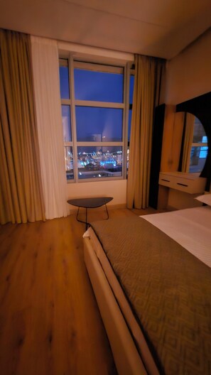 A hotel room with a bed, a small table, a window with curtains, and a view of the city at night. - The Center 101-bedroom apartment with AC in charming Shkodër (Shkodër)