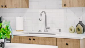 A modern kitchen with a stainless steel sink, wooden cabinets, and a white tiled backsplash. - Evergreen Home - King Bed · Office Room · Near PDX (Gresham)