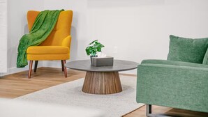 A modern living room with a yellow armchair, a green sofa, and a round coffee table with a plant. - Evergreen Home - King Bed · Office Room · Near PDX (Gresham)