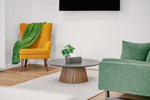 Ein modernes Wohnzimmer mit einem gelben Sessel, einem grünen Sofa und einem runden Couchtisch mit Pflanze.