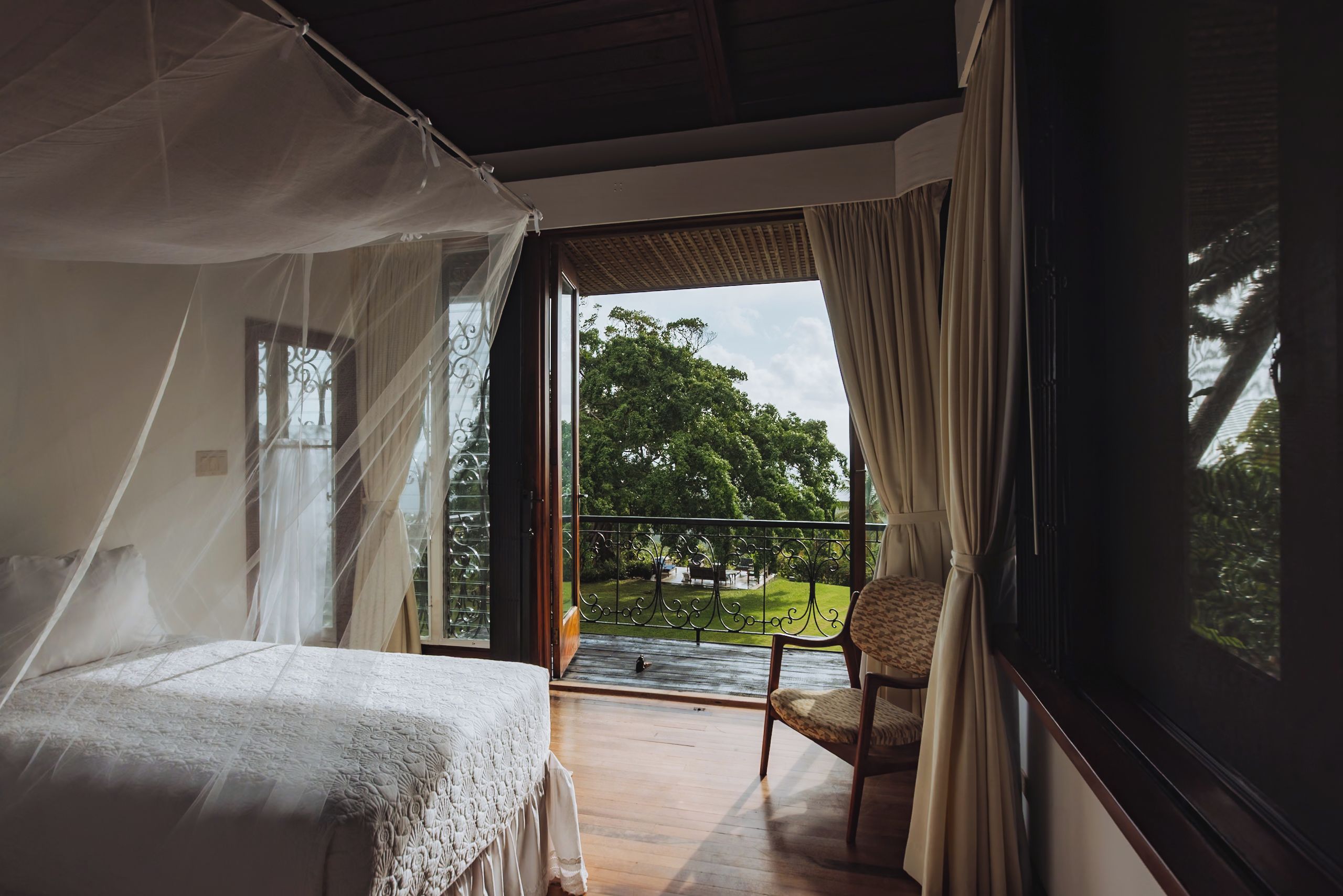 Ein Zimmer mit einem Bett, einem Sessel und einem Balkon mit Blick auf Bäume.