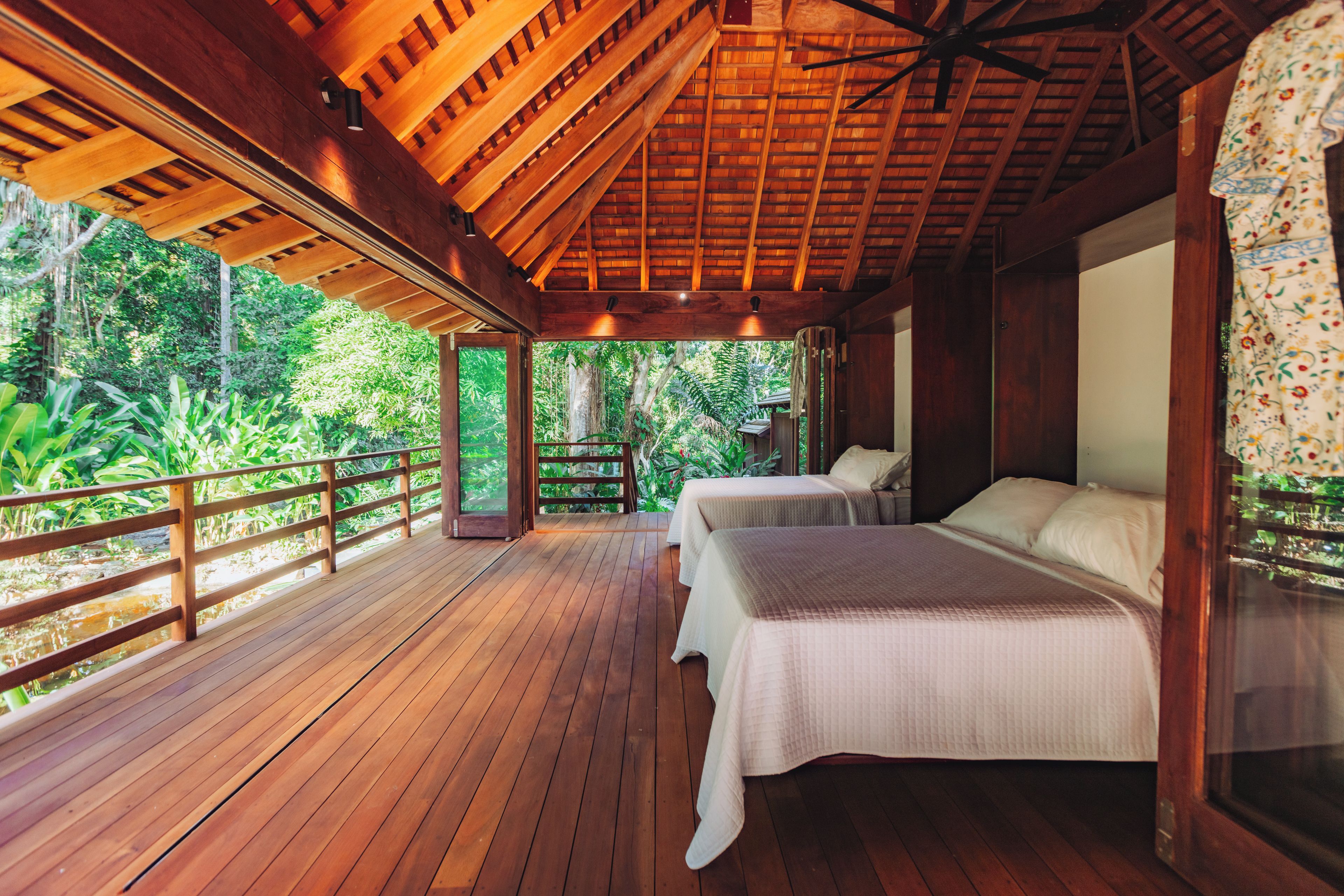 A wooden deck with two beds, a ceiling fan, and a view of lush greenery.