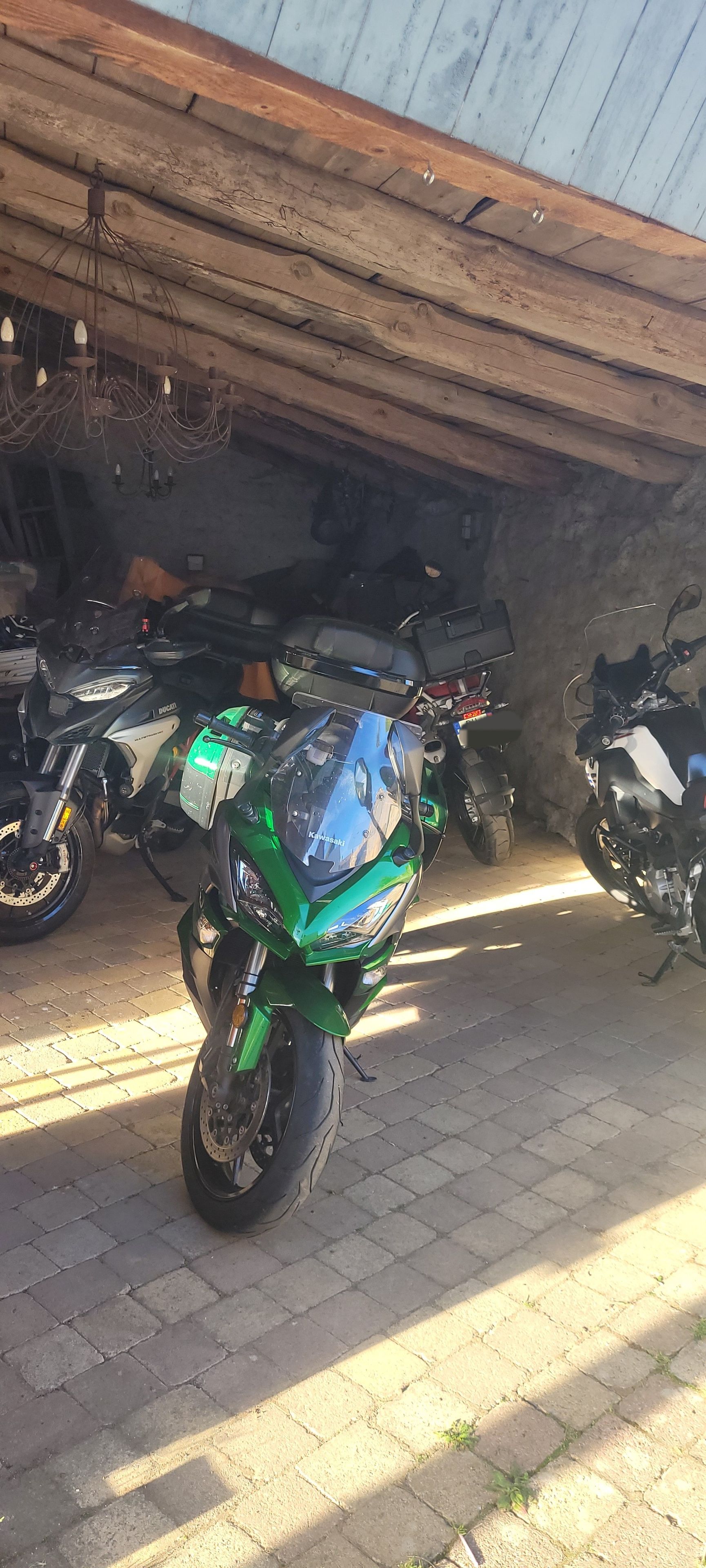 A motorcycle parked in a covered outdoor area with a wooden ceiling and brick flooring.