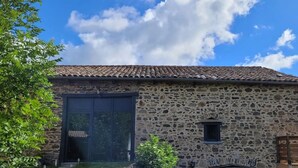 A stone building with a tiled roof, a large garage door, and a small window. - “Cézallier Room” Guest Suite with Private Terrace and Jacuzzi (Soulages)