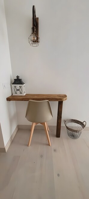 Habitación minimalista con una mesa de madera, una silla, un aplique de pared y un pequeño farol blanco.