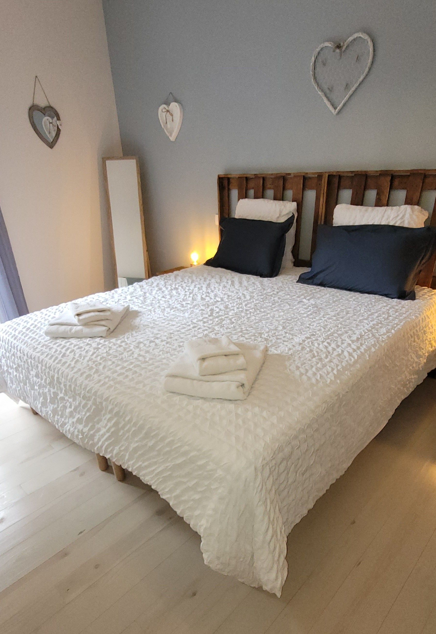 A bed with a white textured bedspread, two pillows, and folded towels on a wooden headboard.