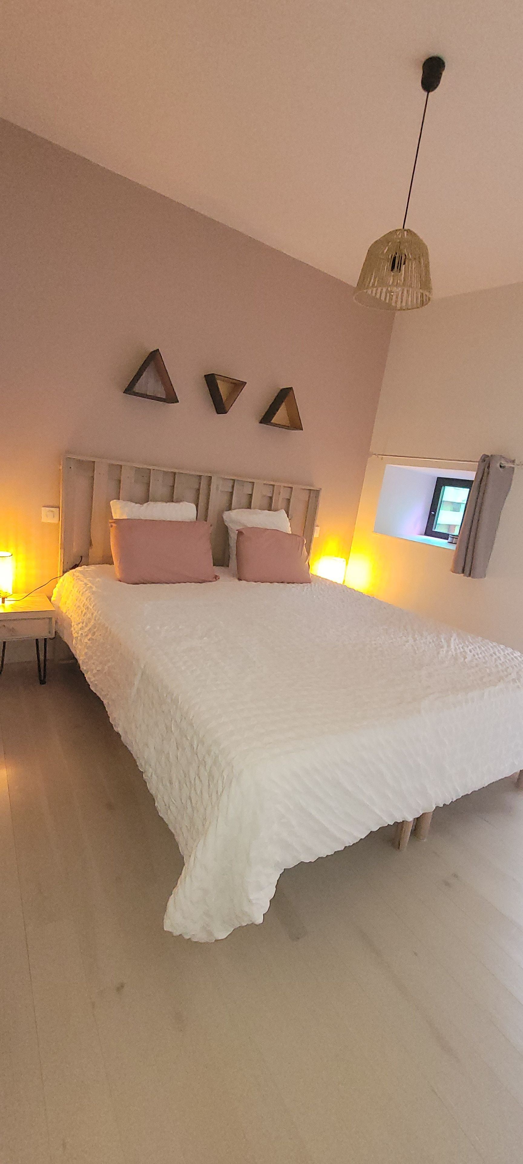 Een slaapkamer met een groot bed, een nachtkastje, een aan de muur bevestigde televisie en een hanglamp.