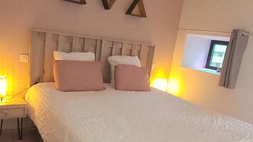 Een slaapkamer met een groot bed, een nachtkastje, een aan de muur bevestigde televisie en een hanglamp.