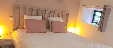 Une chambre à coucher avec un grand lit, une table de chevet, un téléviseur fixé au mur et un luminaire suspendu.