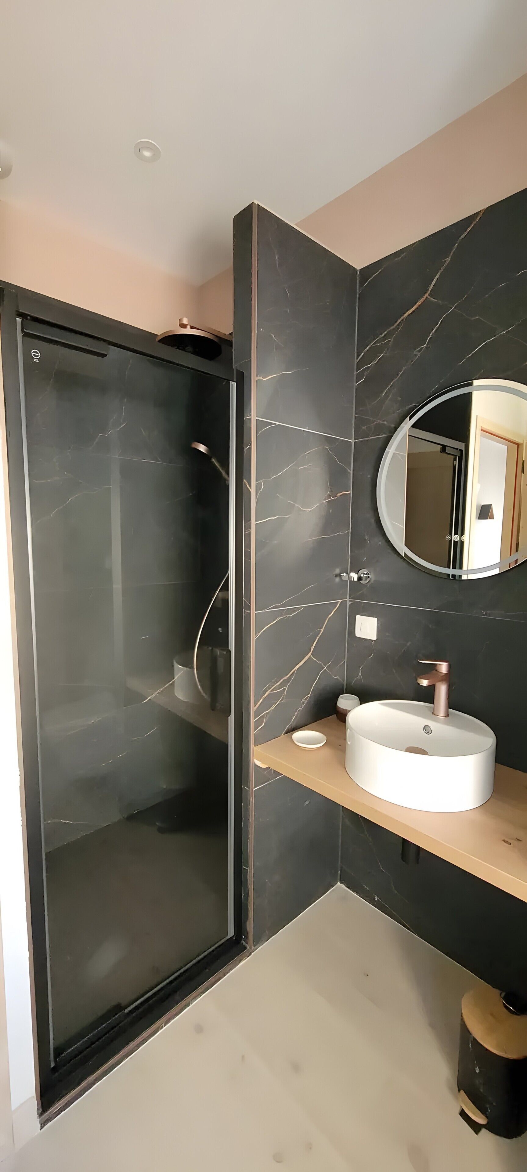 Een moderne badkamer met een douchecabine van glas, een ronde spiegel en een wit wastafelmeubel met een koperen kraan.