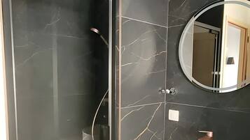 Een moderne badkamer met een douchecabine van glas, een ronde spiegel en een wit wastafelmeubel met een koperen kraan.