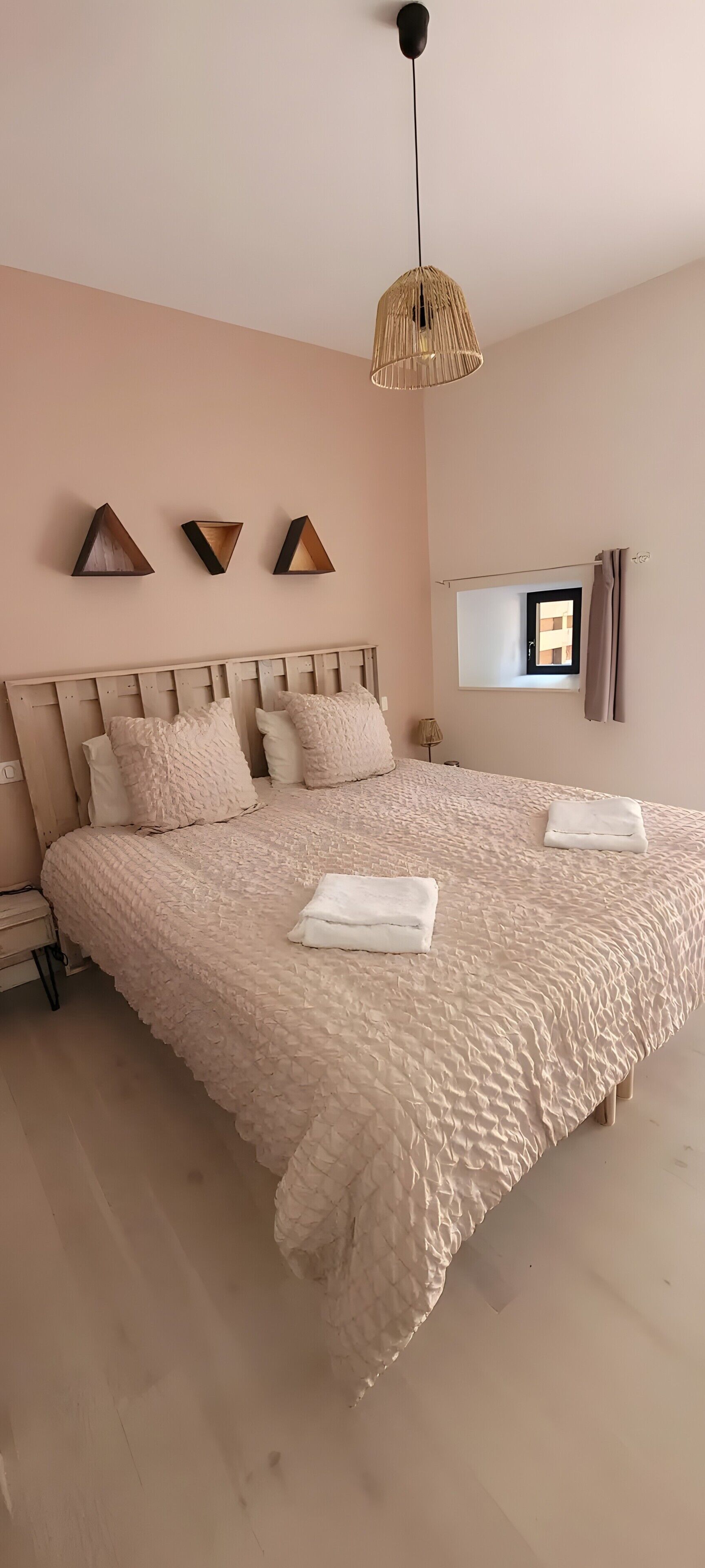 A bedroom with a large bed, a hanging light fixture, and a window with curtains.