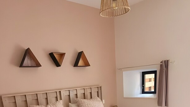 A bedroom with a large bed, a hanging light fixture, and a window with curtains.