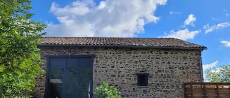 Un edificio de piedra con techo de tejas, un amplio portón de garaje y un pequeño ventanal.