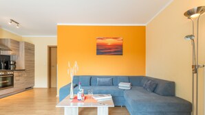 Una sala de estar moderna con un sofá azul, una mesa de centro y un cuadro de una puesta de sol.