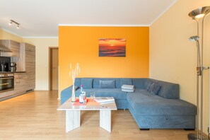 Een moderne woonkamer met een blauwe bank, een salontafel en een schilderij van een zonsondergang.