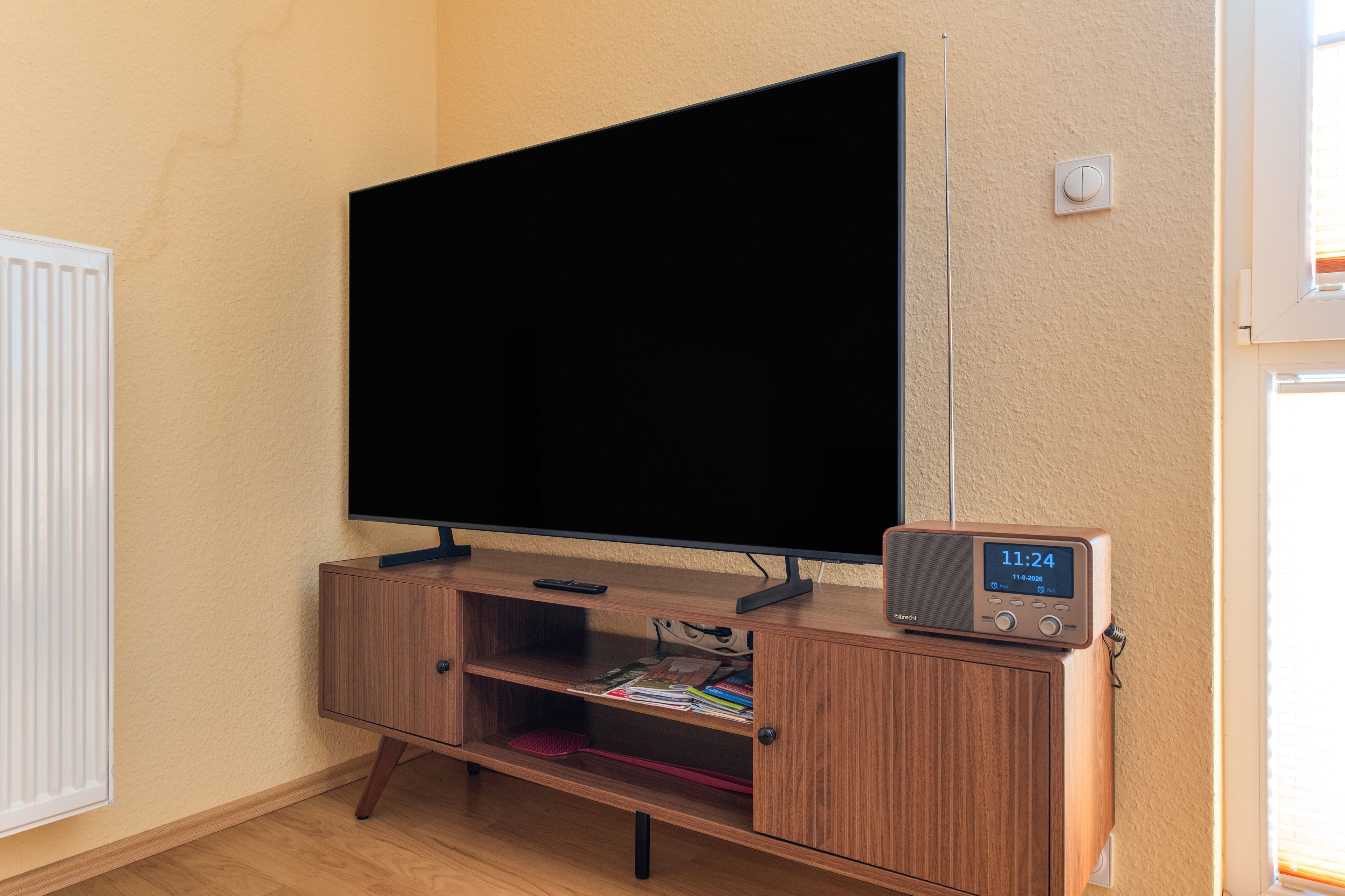 Un televisor de pantalla plana montado sobre un soporte de madera, con un reloj digital que marca las 11:24.