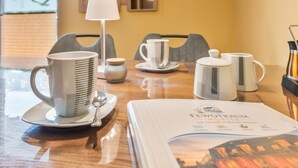 Habitación de hotel con una mesa de comedor dispuesta con tazas blancas, una cuchara y un menú.